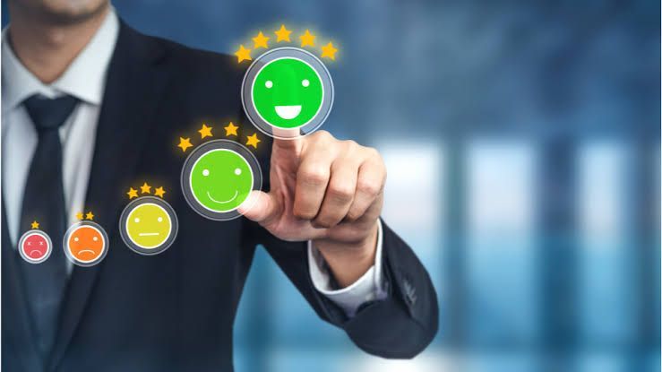 Hand selecting a smiling face icon from three rating icons on a blurred background