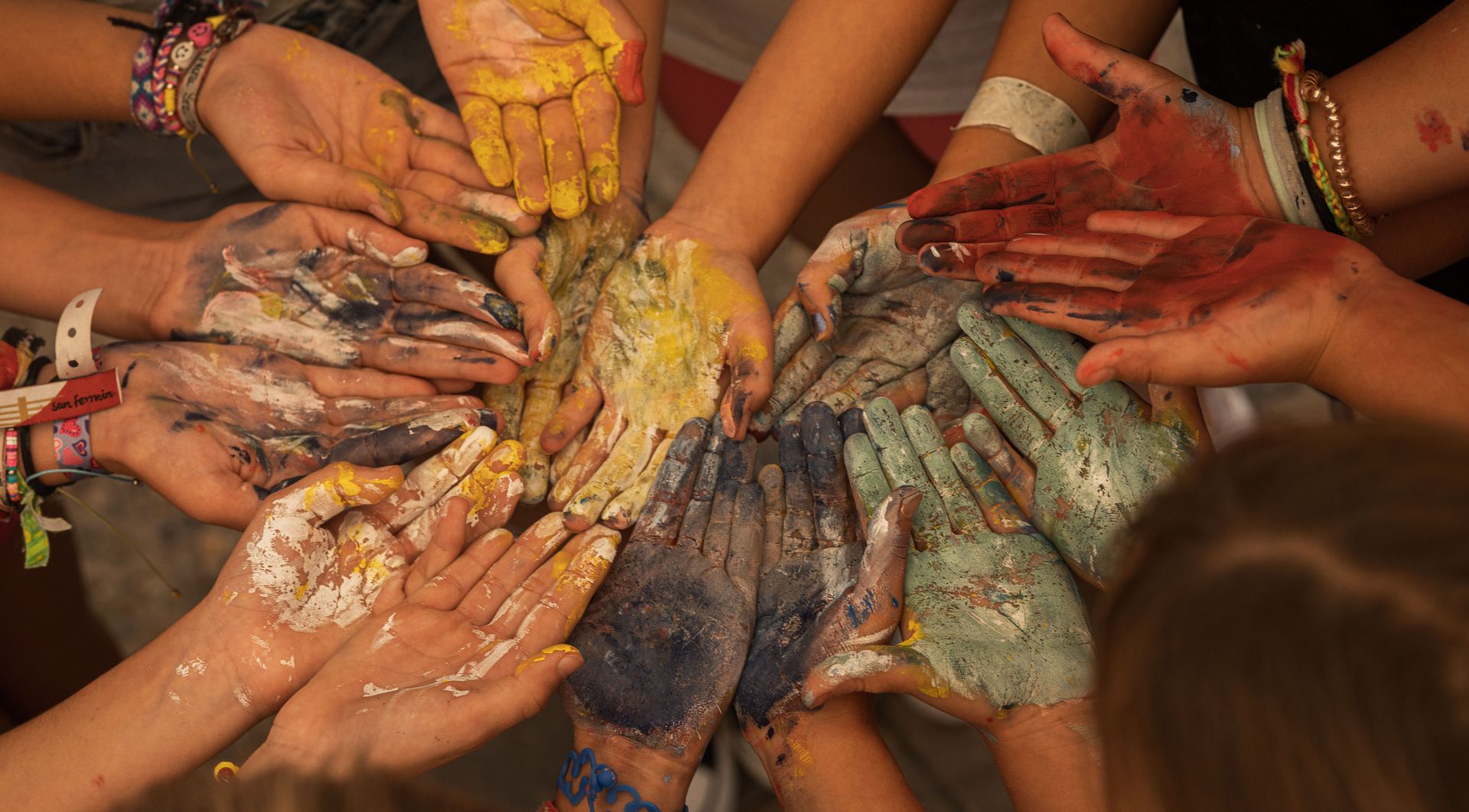 Hands with colorful paint gathered in a circle over a wooden floor