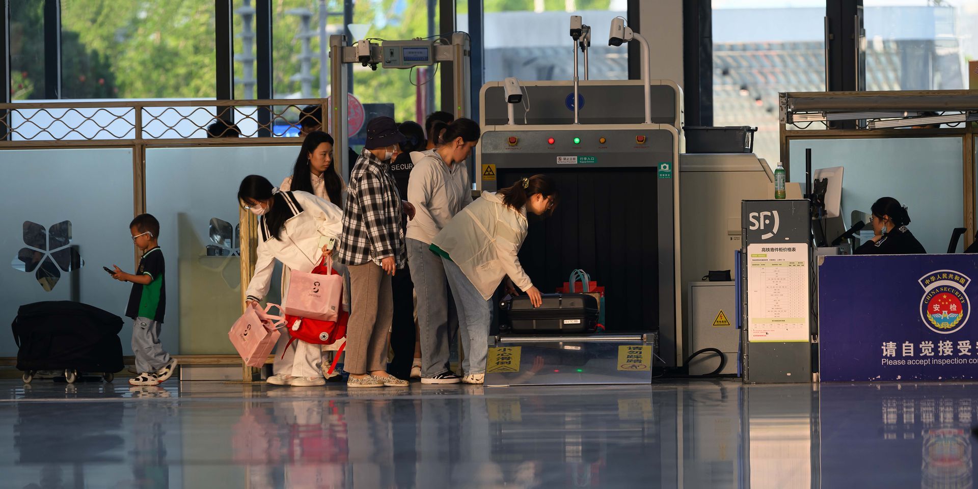 Travelers queue at an airport security checkpoint with luggage and metal detectors.