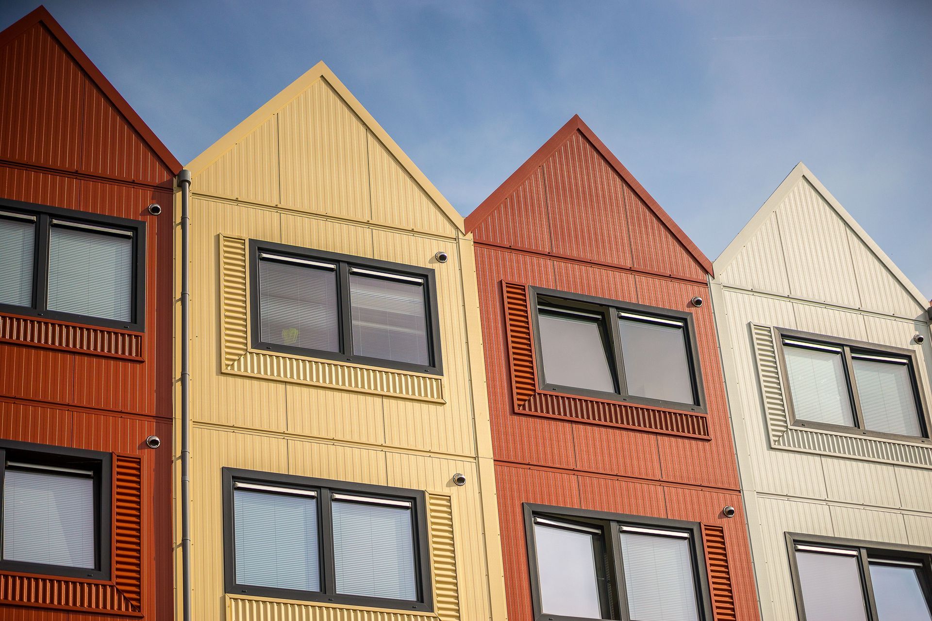 Colorful row of modern houses with triangular roofs and large windows under a blue sky