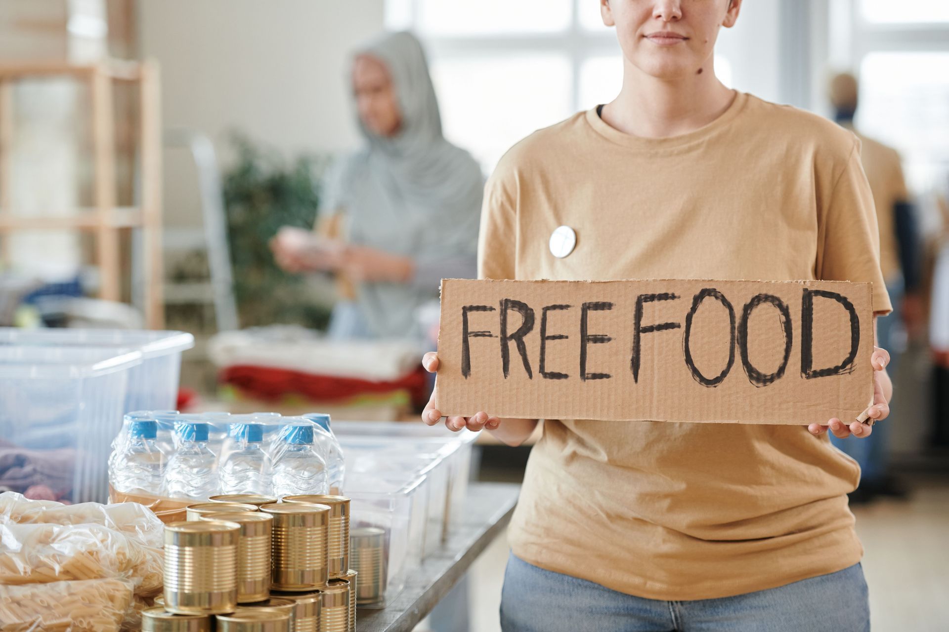Person holding a “FREE FOOD” sign at a community food distribution table