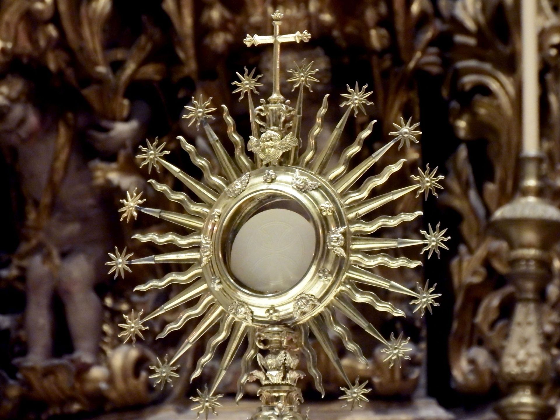 Gold sunburst religious monstrance with a circular center against an ornate altar background