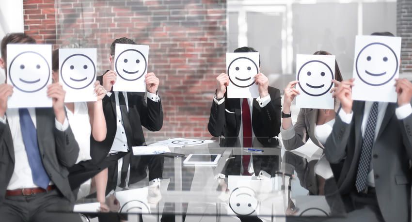 A group of business people are holding up smiley faces in front of their faces.