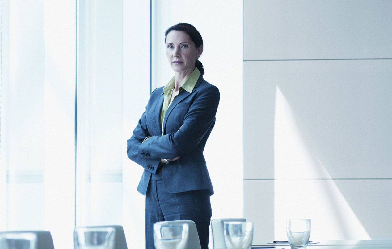 Businesswoman standing in a bright conference room with arms crossed, near water glasses on a table