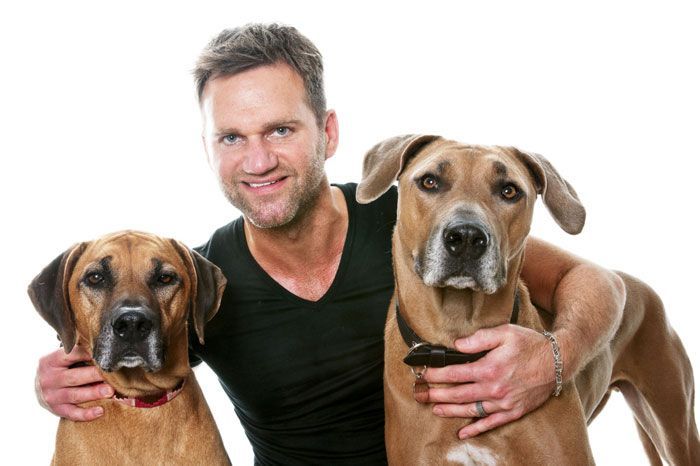 A man is hugging two brown dogs on a white background.