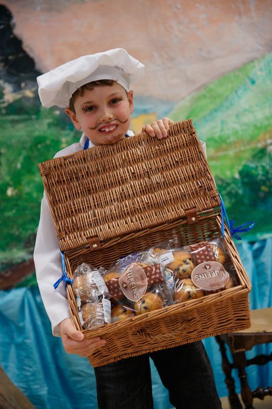 A young boy dressed as a chef is holding a basket of food.