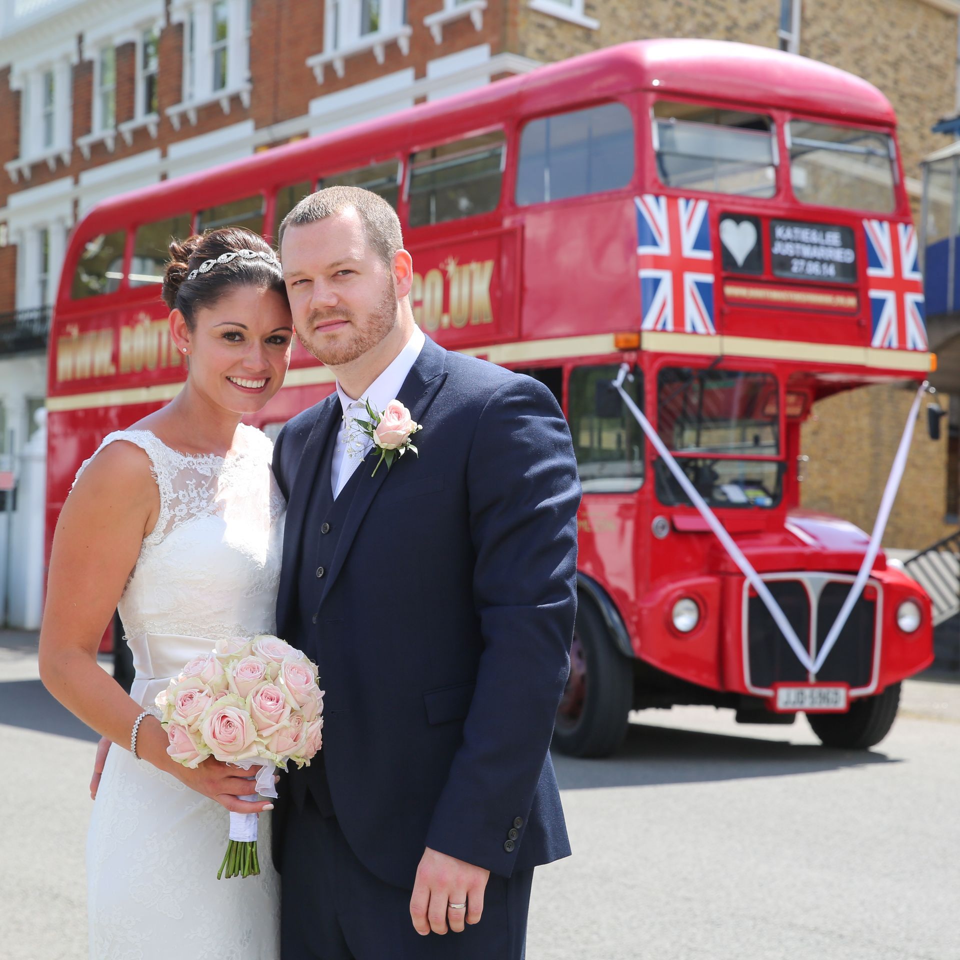 A bride and groom pose in front of a red double decker bus