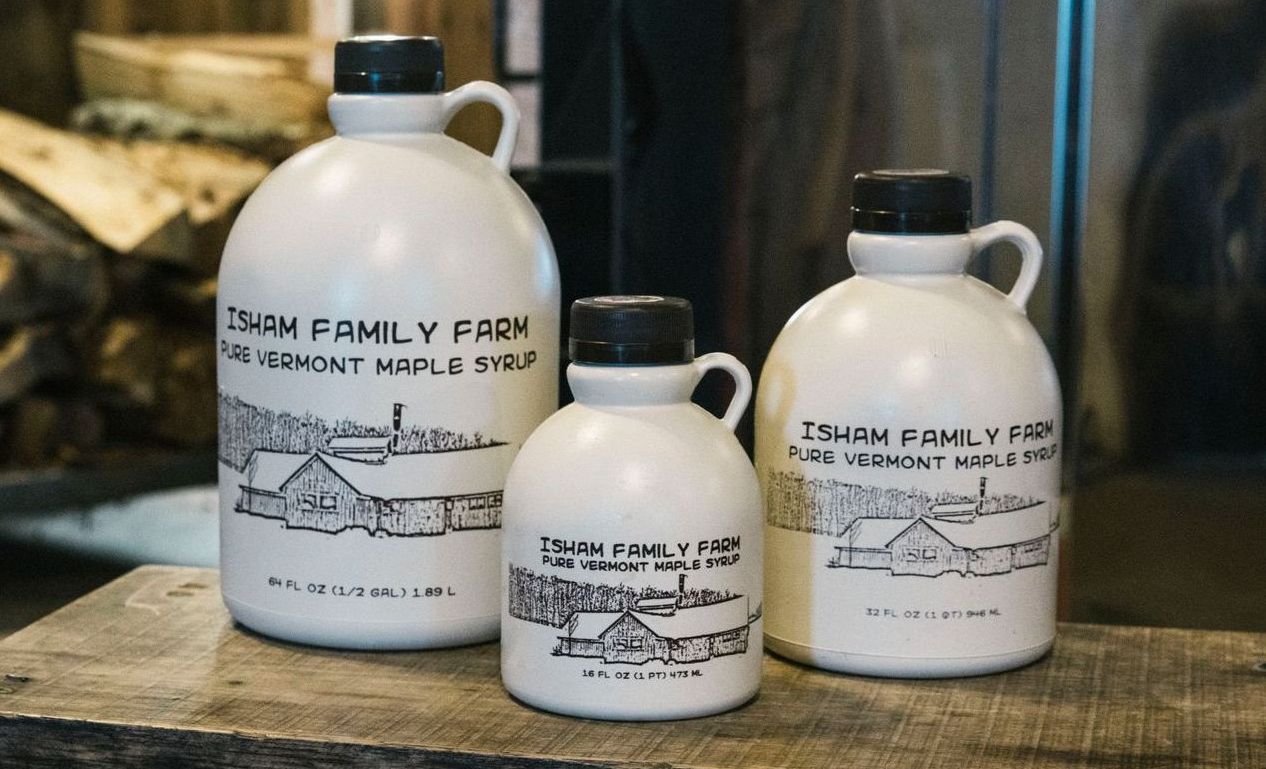 Vermont maple syrup bottles from Isham Family Farm in 16, 32, and 64 oz sizes on display atop a rustic wooden table.