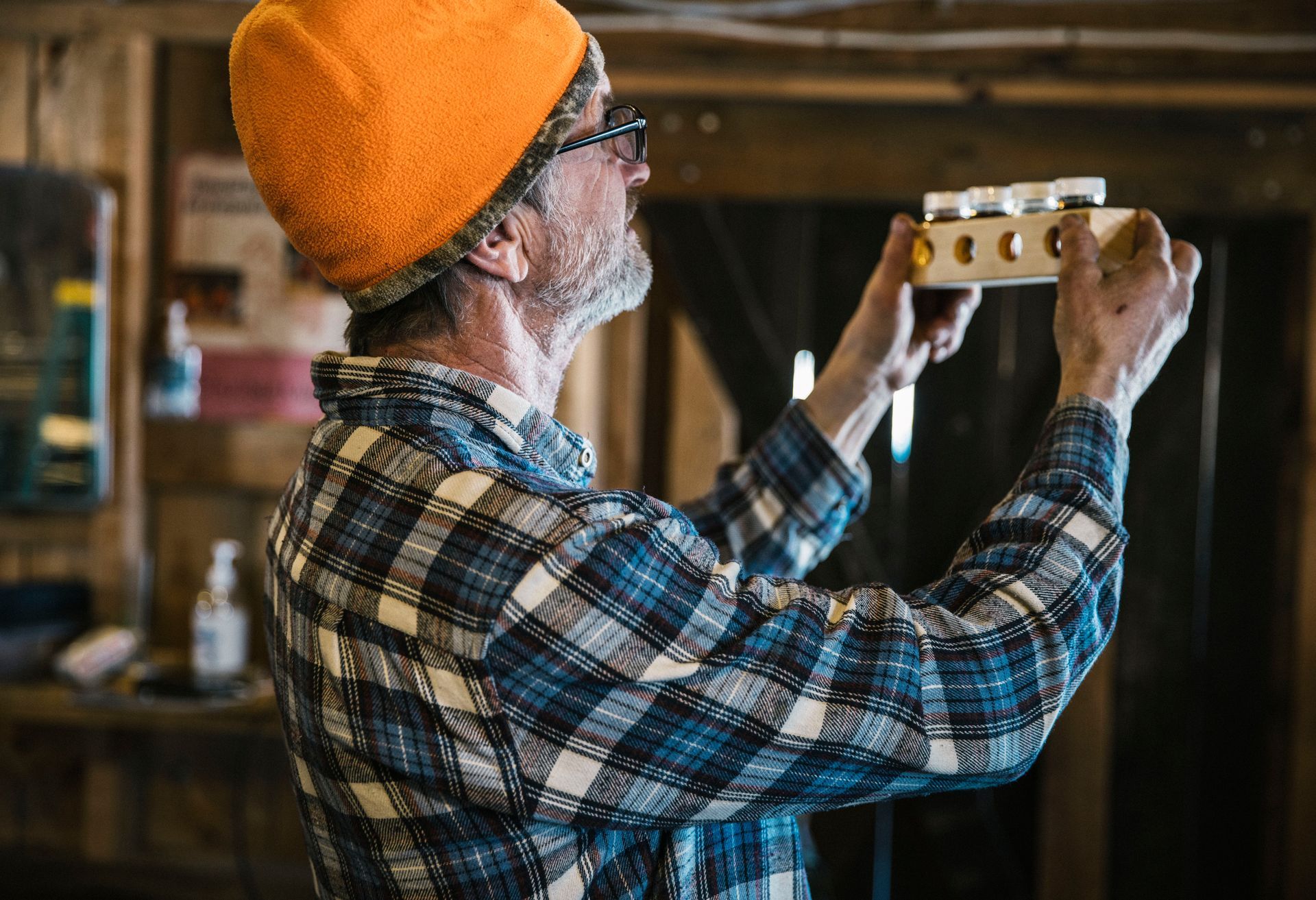 Vermont sugarmaker at Isham Family Farm inspecting maple syrup color grades in a rustic sugarhouse.