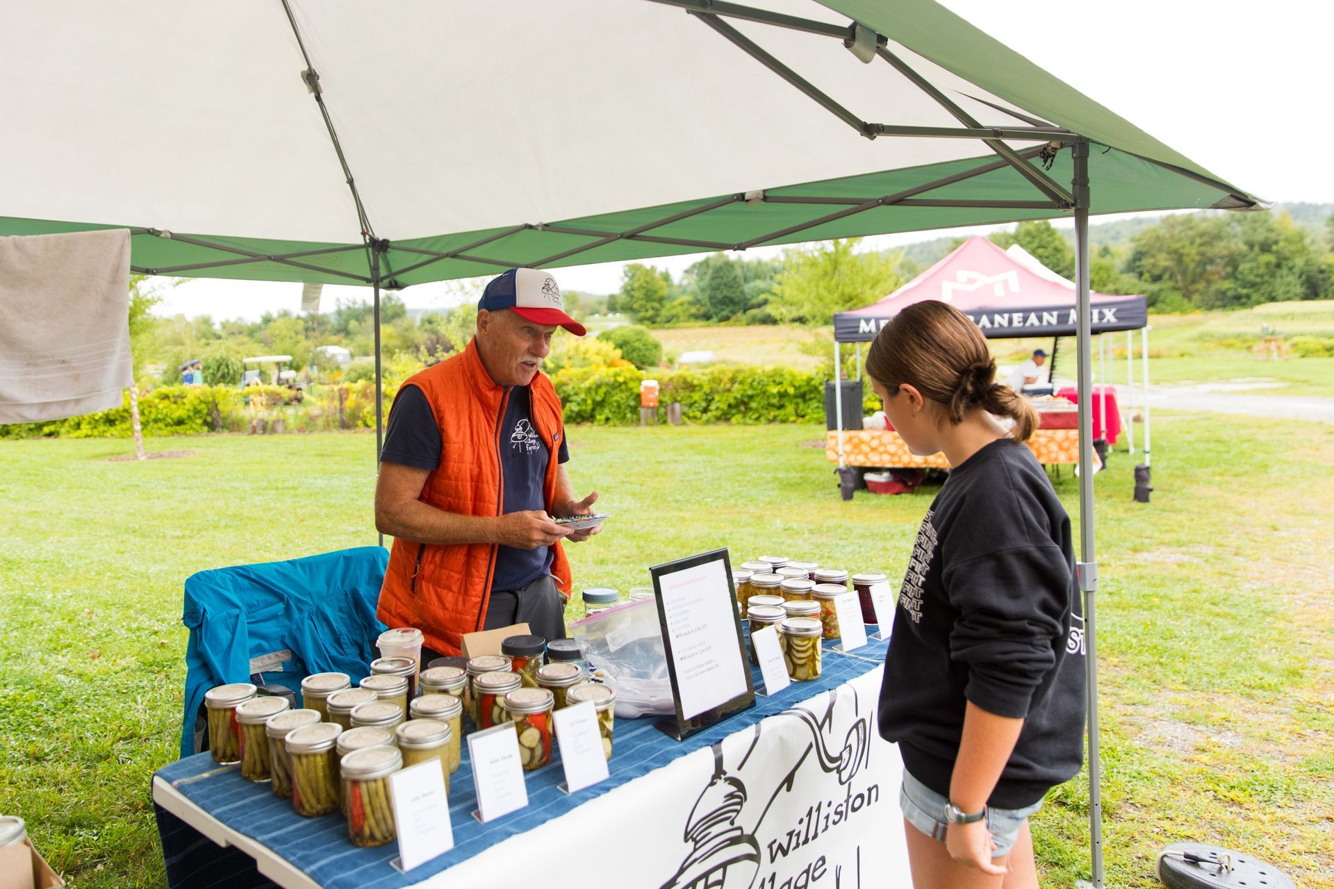 Local pickle vendor talking to a customer at isham family farmer's market in Vermont