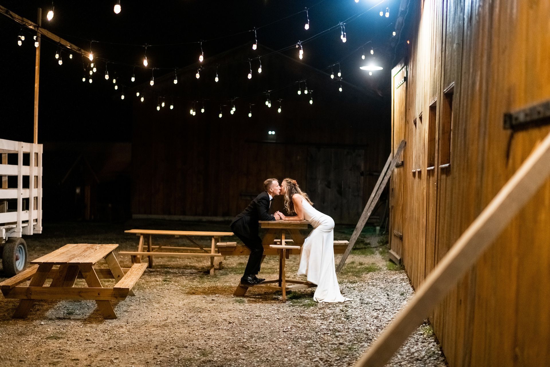 A bride and groom are kissing at a picnic table at night.