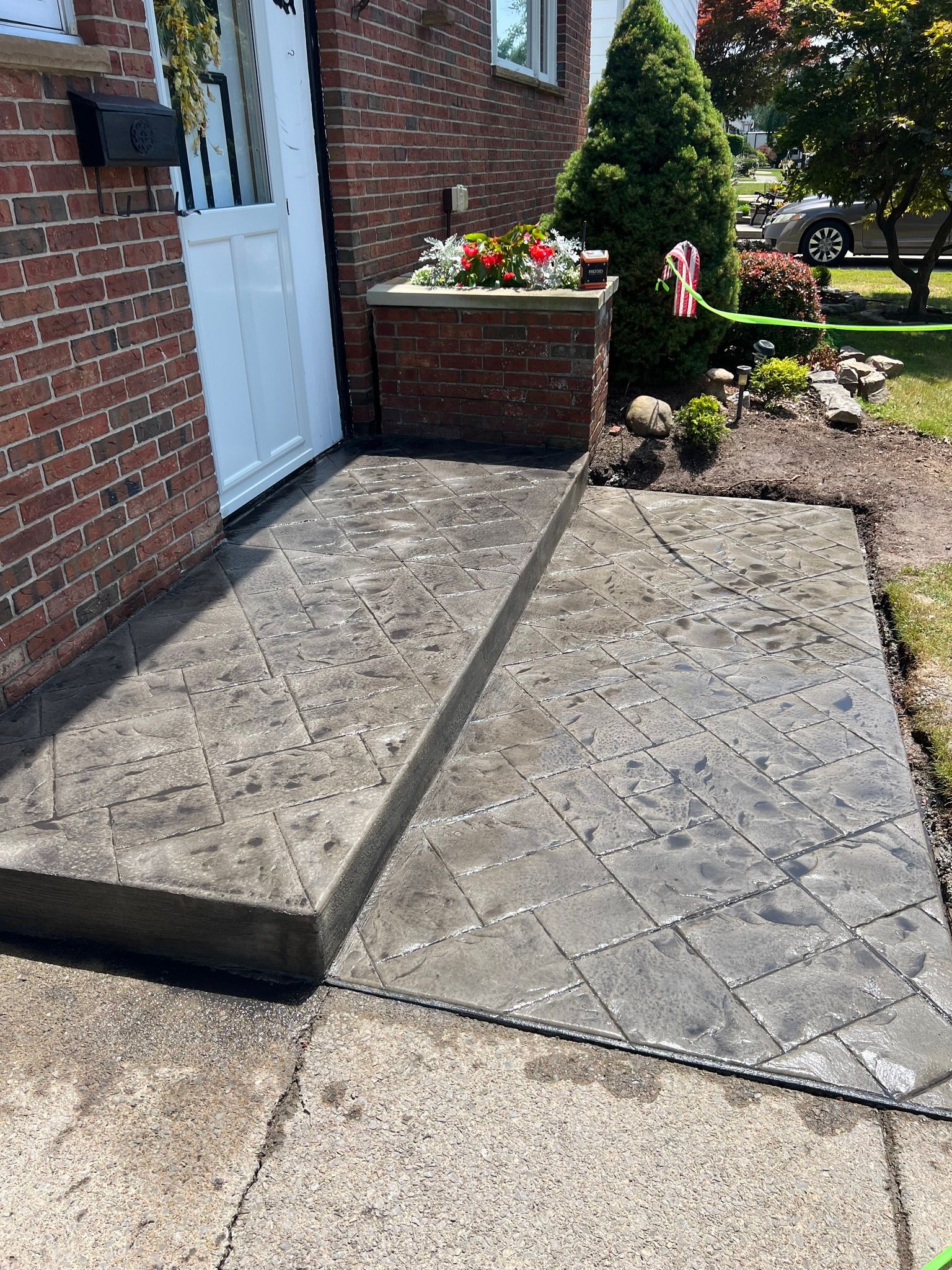 A stamped, dark gray concrete entryway leading to a white door on a brick house, featuring a small raised stoop.