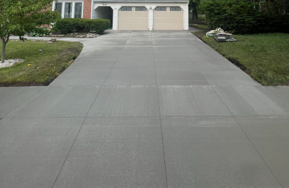 A view from the bottom of a new, gray concrete residential driveway leading to a two-car garage.