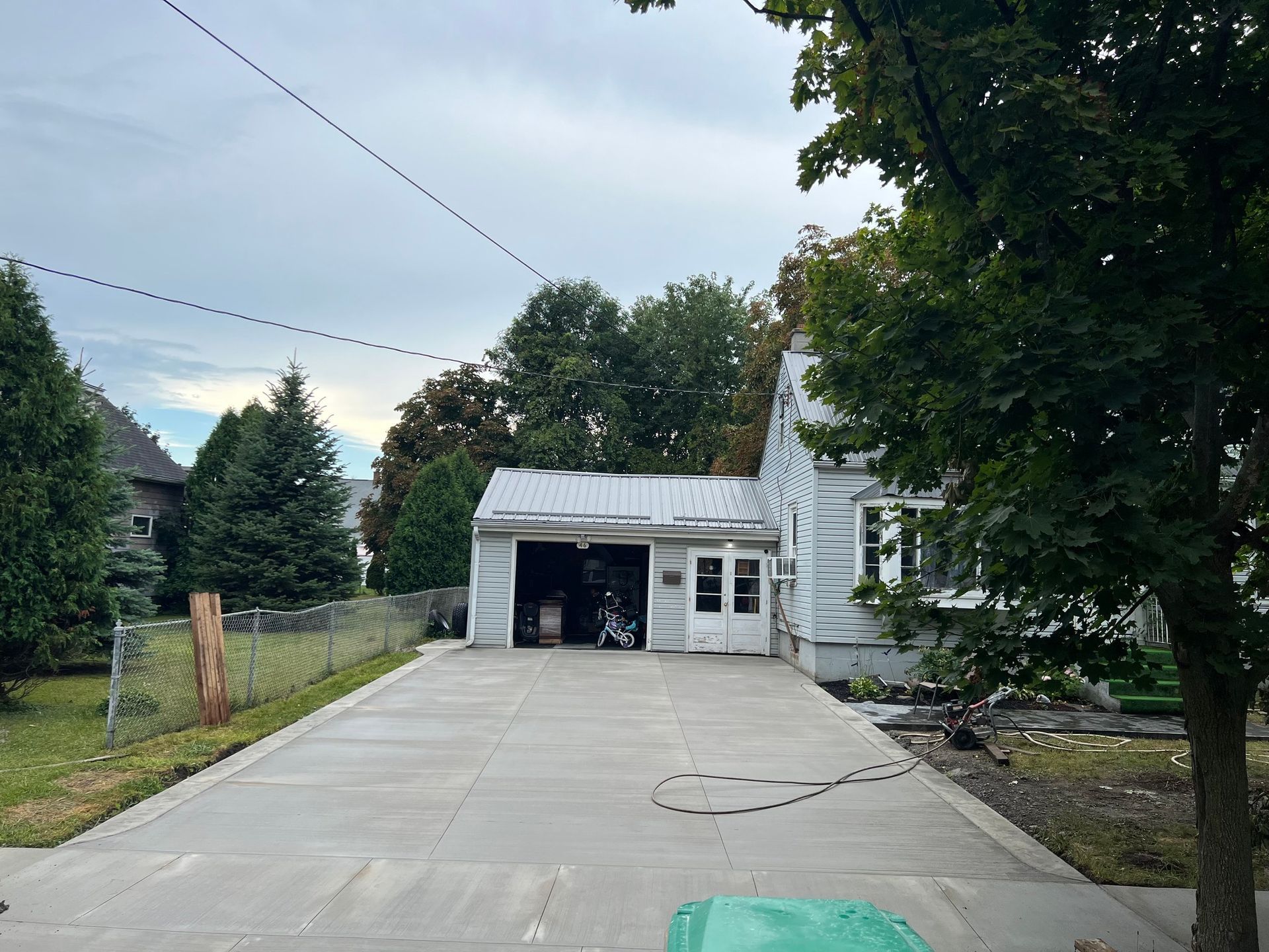 A paved driveway leads to a white house with an open garage and a partial view of a green lawn and trees.