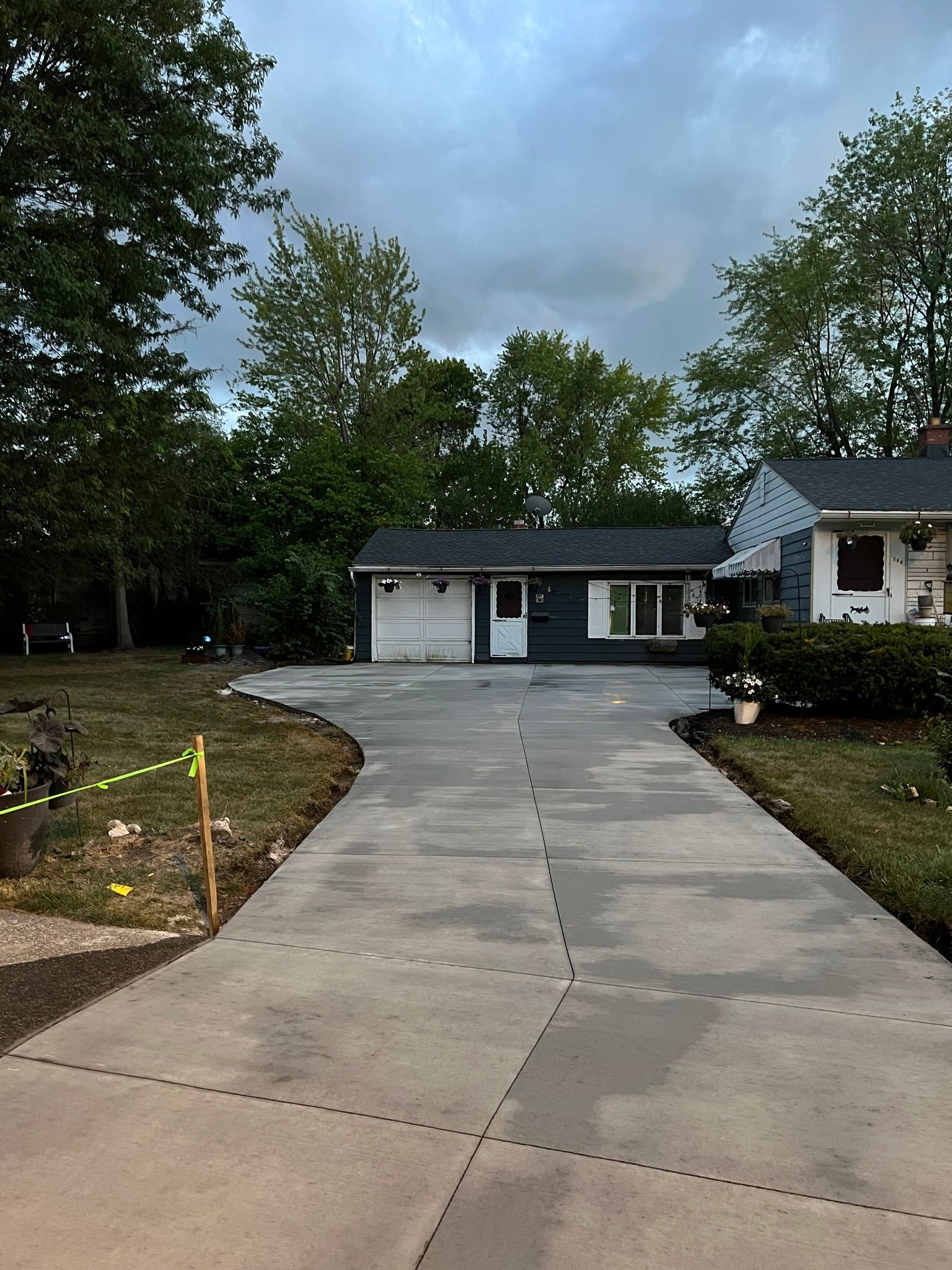 A newly paved concrete driveway leads toward a one-story detached garage under a cloudy sky.