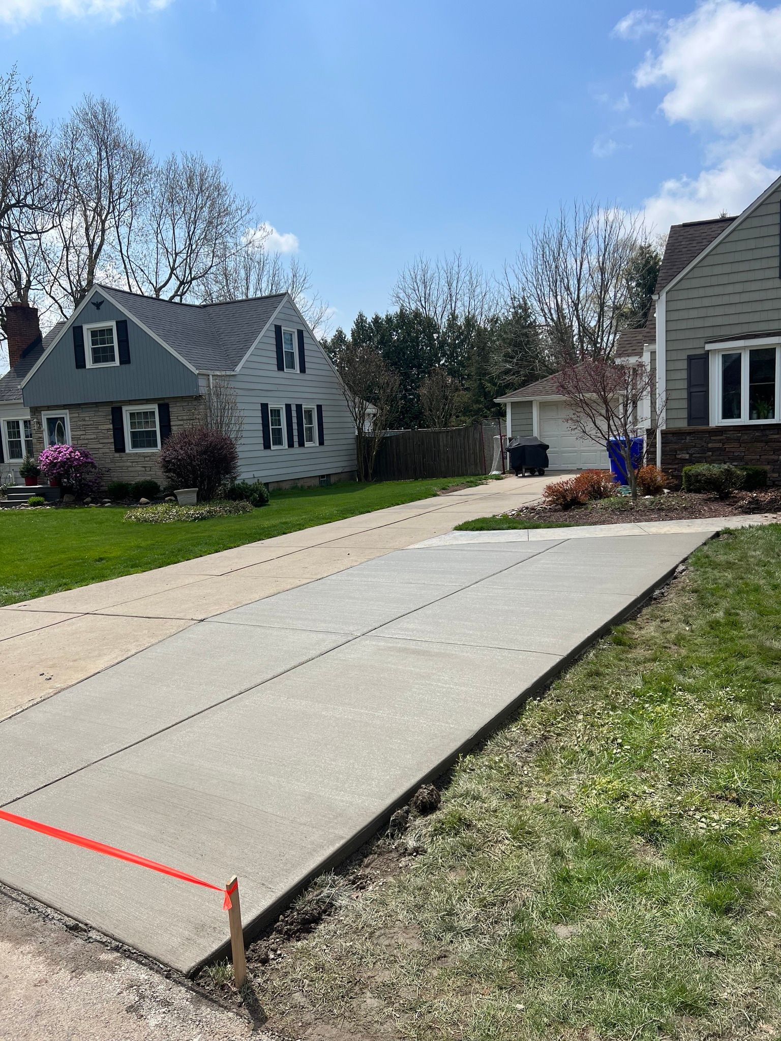 A newly poured concrete driveway strip next to an older driveway, bordered by a wooden stake and orange string.
