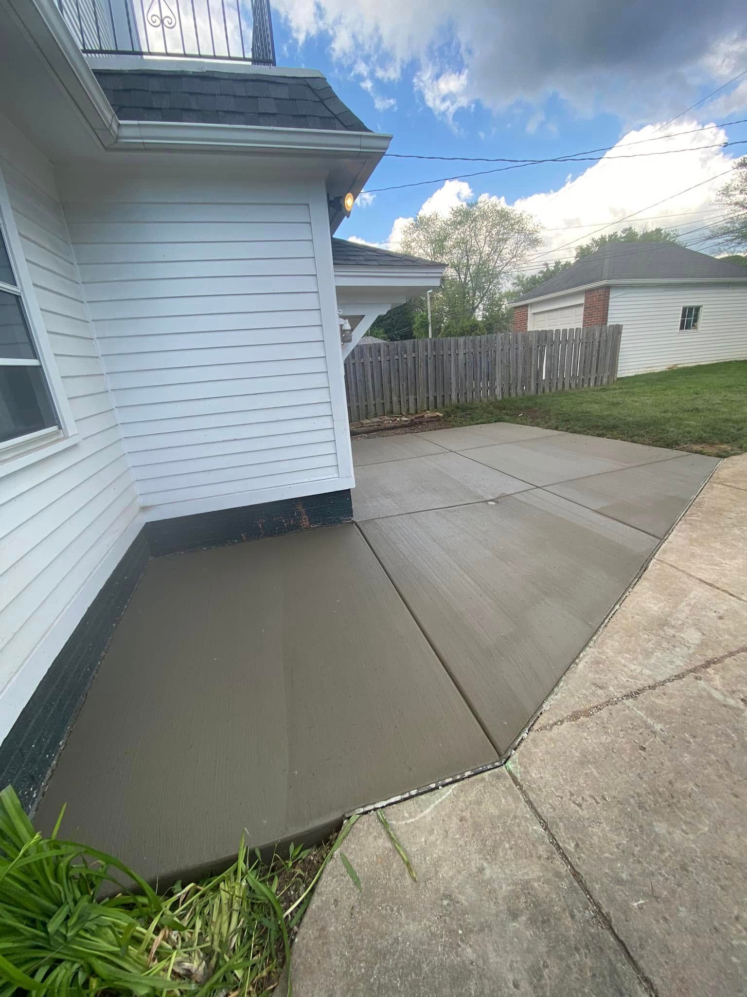 A newly poured gray concrete patio slab next to a white house, meeting an older, weathered concrete walkway.