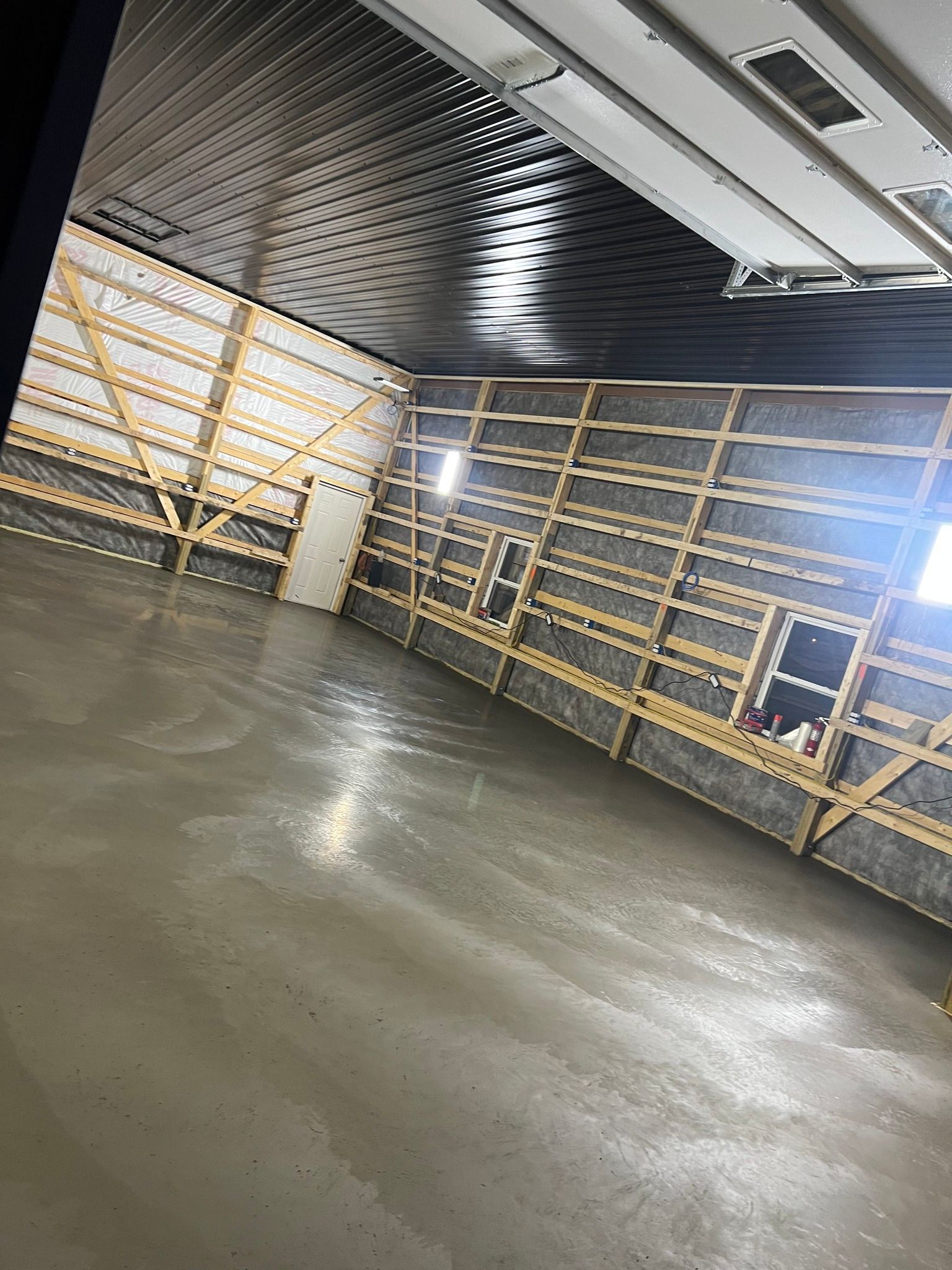 A wide-angle view of a garage interior with a dark patterned ceiling, bare wooden wall framing, and a smooth concrete floor.