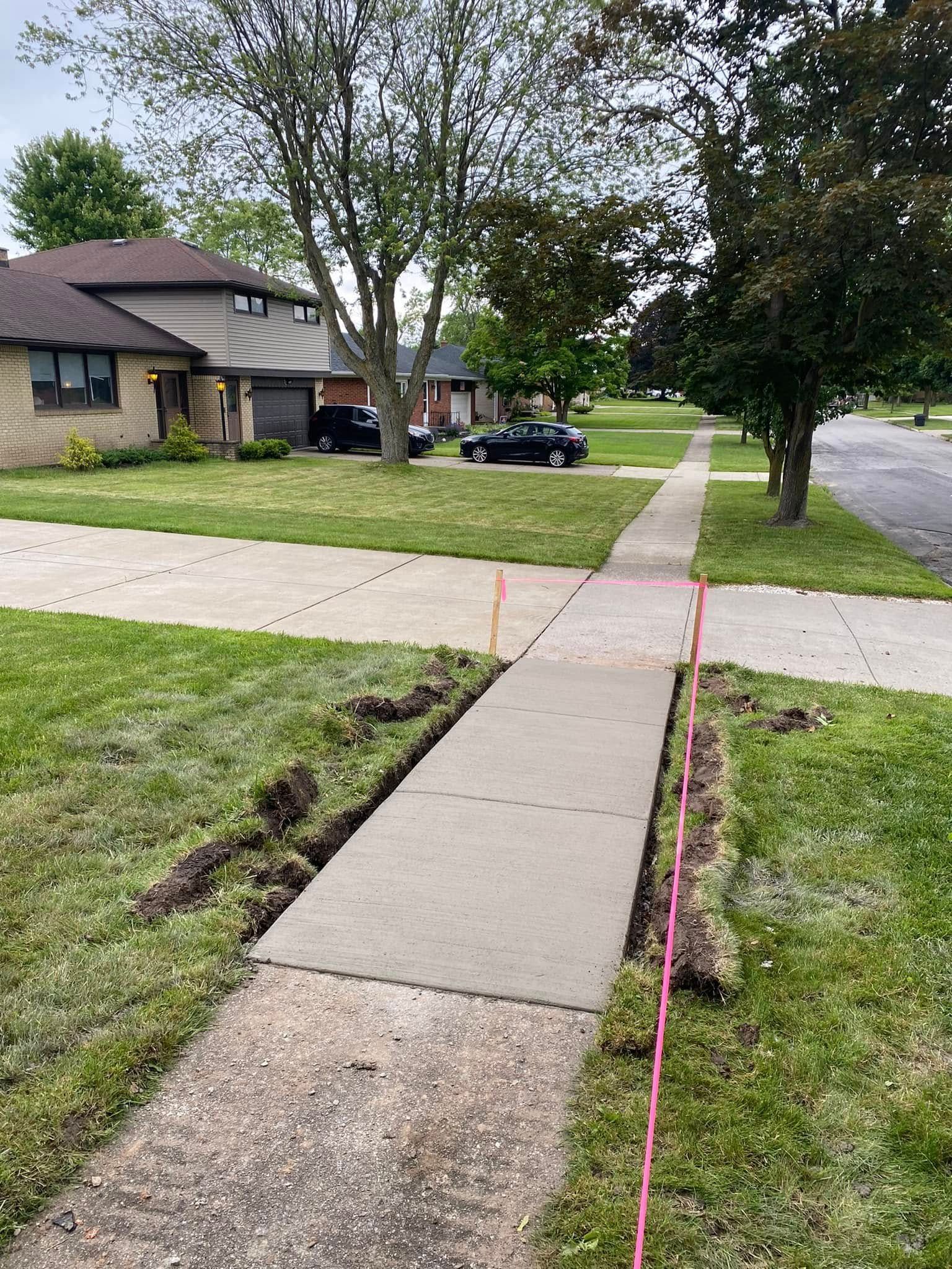 A newly poured concrete sidewalk section in a residential neighborhood, marked by orange string lines along the edges.