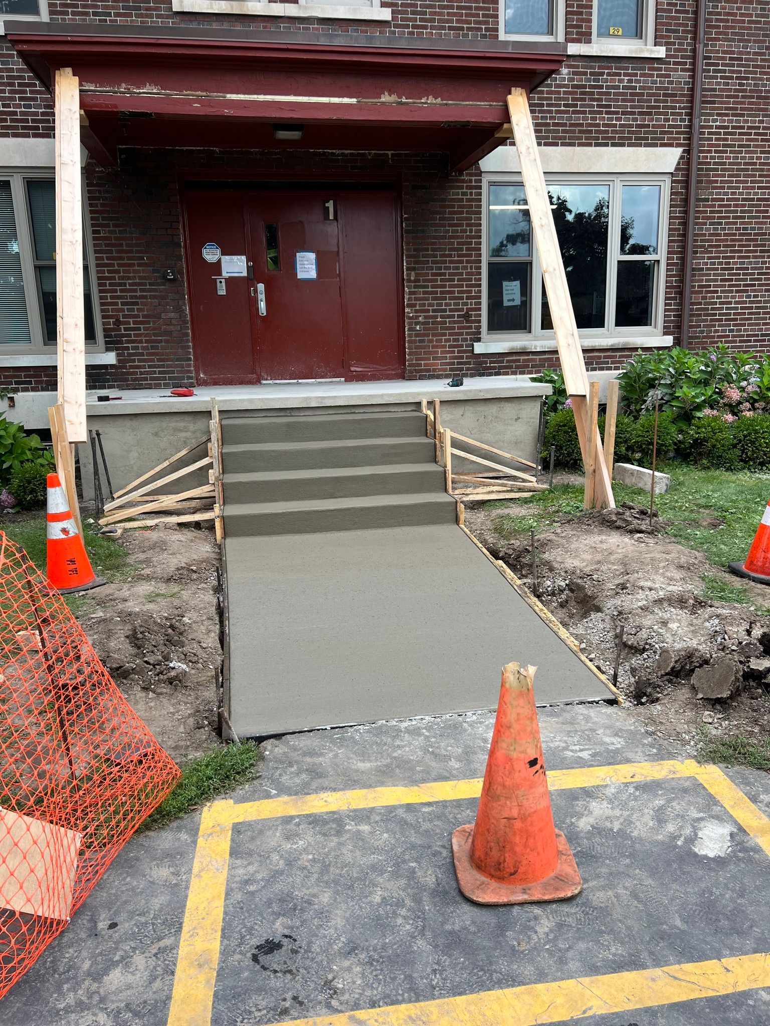 Newly poured concrete steps and a walkway leading to a building entrance with temporary wooden support beams.