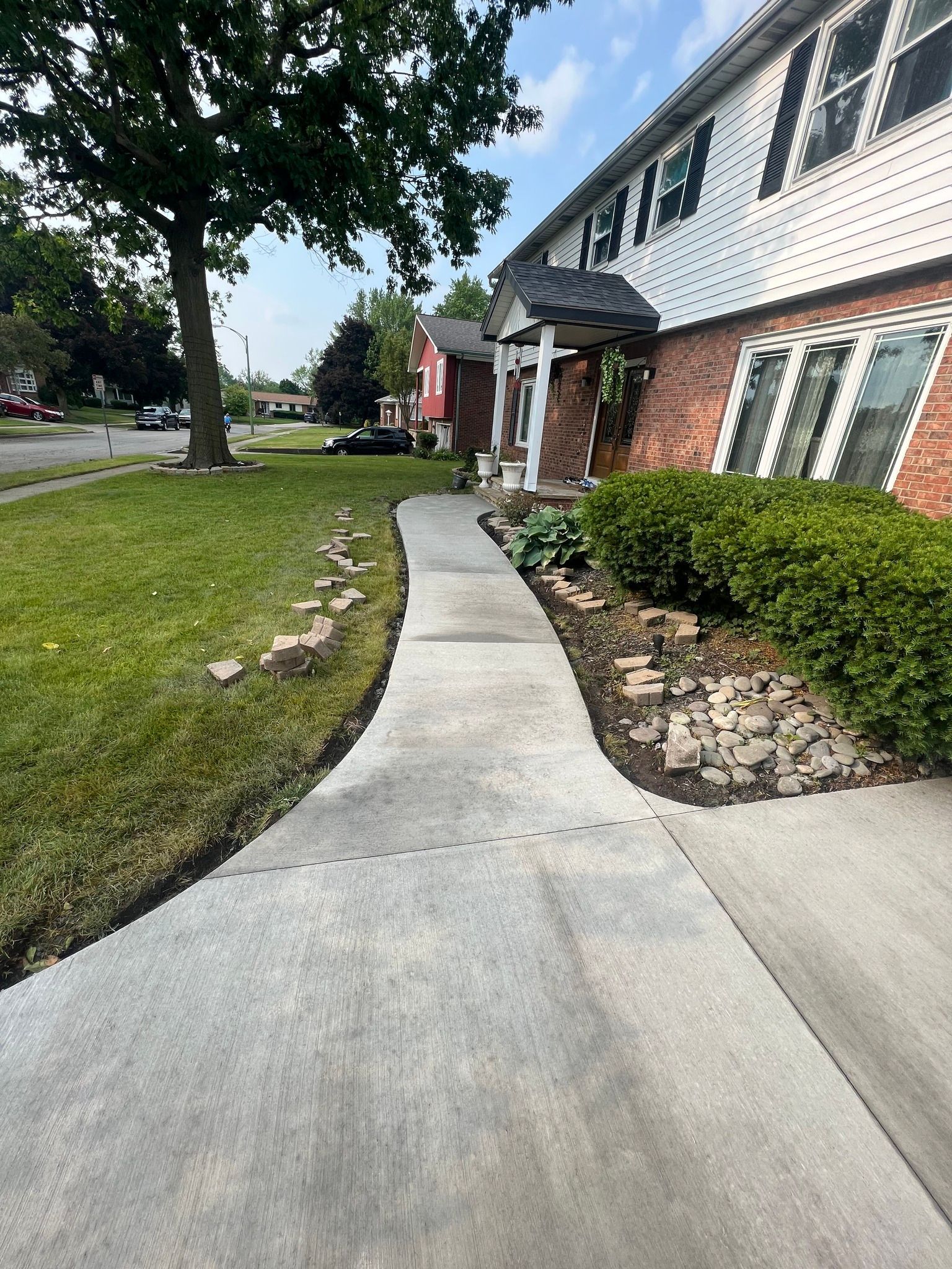 A concrete walkway leading to the front entrance of a multi-story house with a brick and white siding facade.