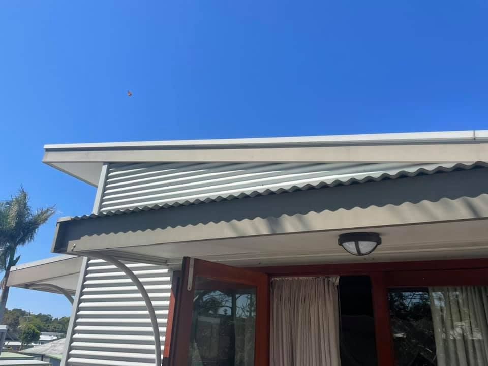 Exterior of a building with a blue sky. Horizontal gray siding, corrugated roof, and open double doors.