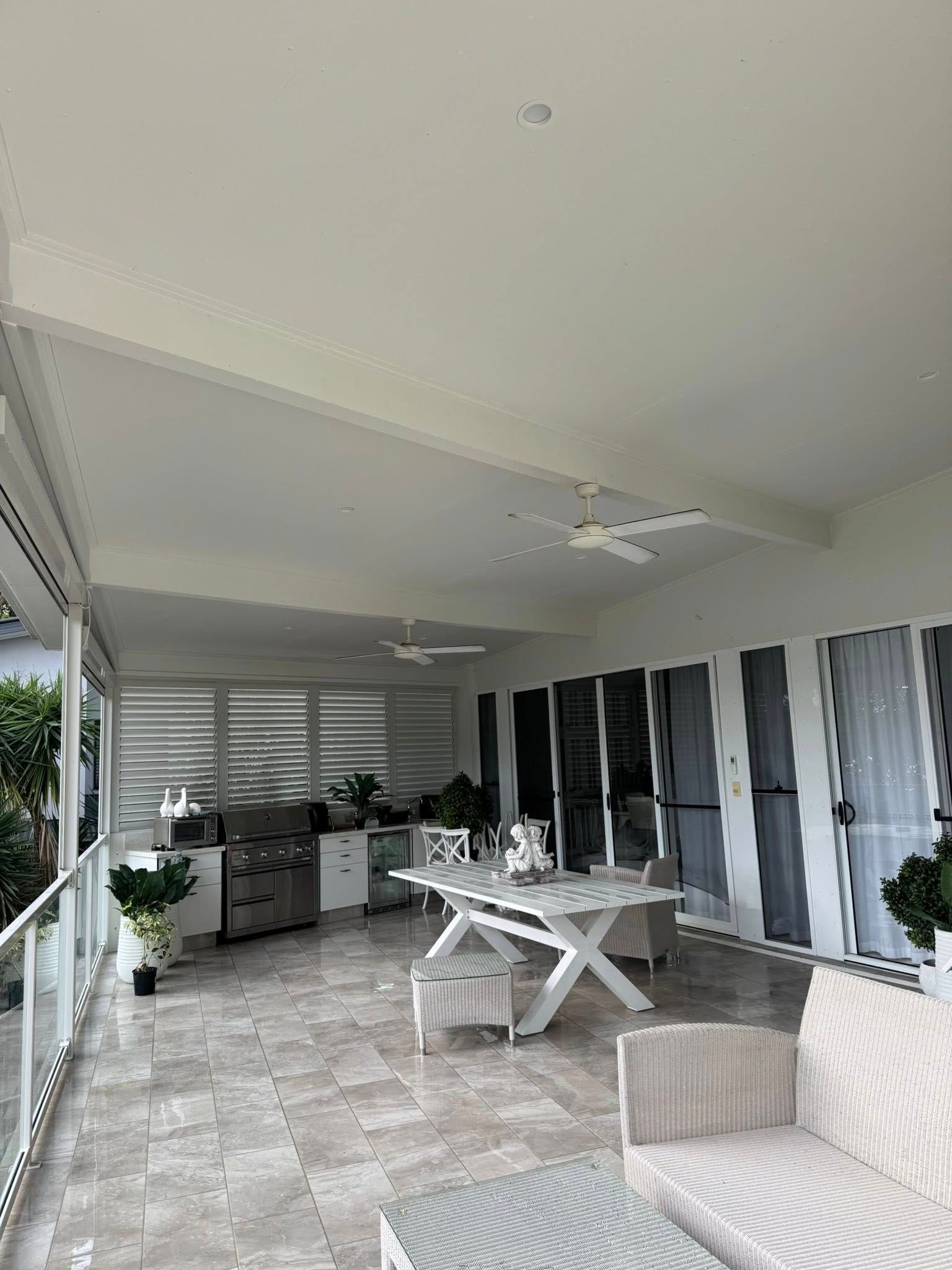 Patio with white ceiling, outdoor kitchen, white table, and seating.