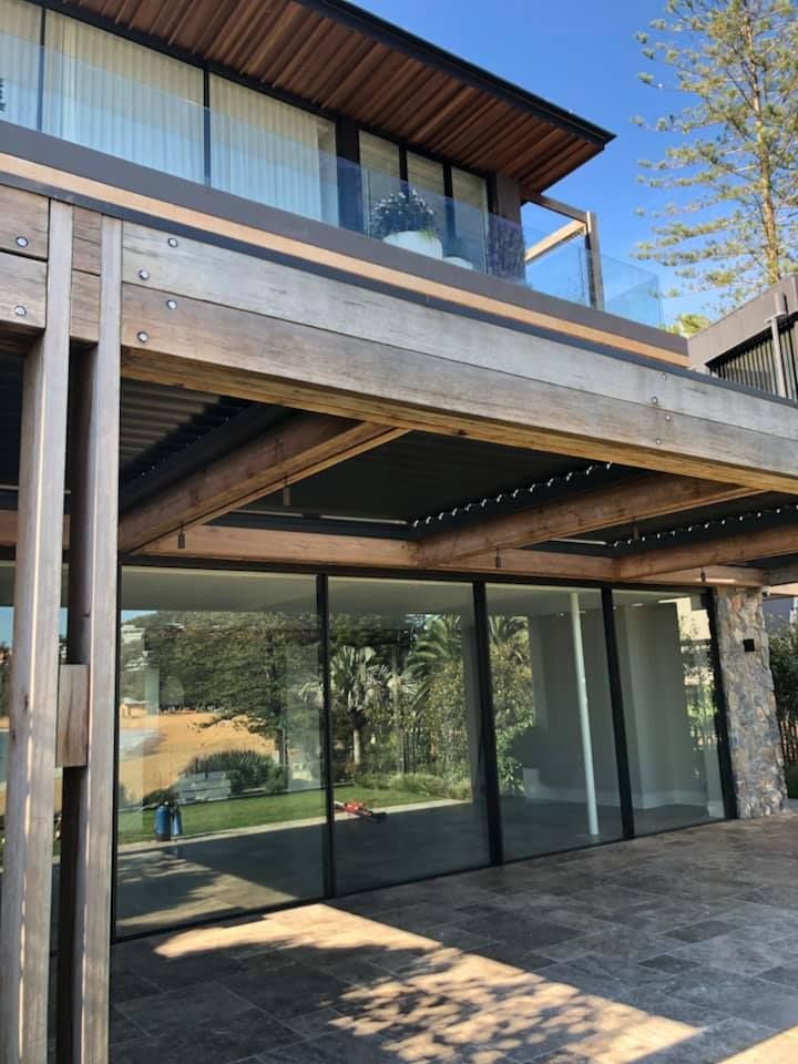 Modern home exterior with wooden beams, glass windows, and a tiled patio.