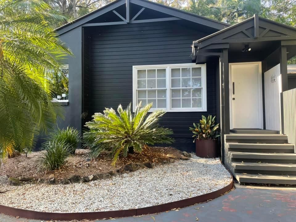 Black house with white window, door, and stairs. Gravel path and plants in front.
