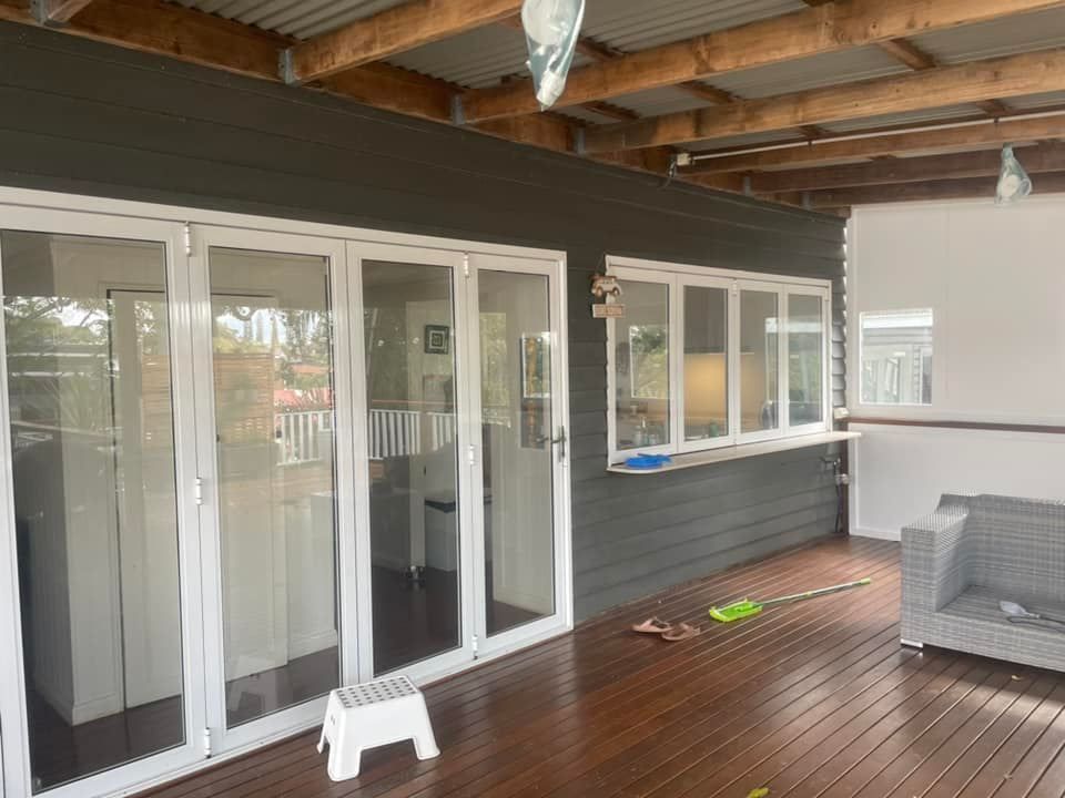 Dark gray building with white trim, bi-fold doors, and a pass-through window on a wood deck.