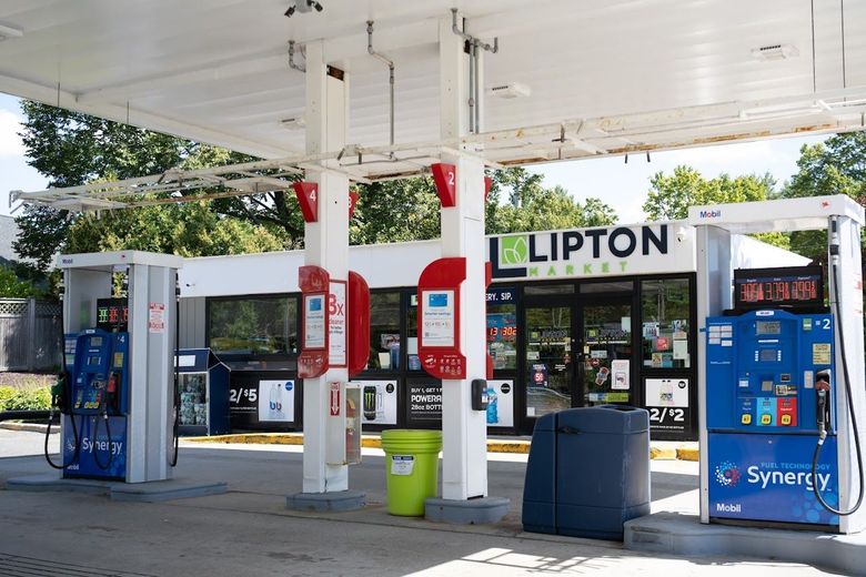 Gas station with blue and red pumps, a green trash can, and a Lipton Pharmacy in the background.