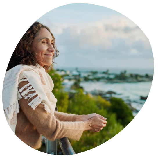 Woman in a white shawl looking out over a coastal landscape at sunset