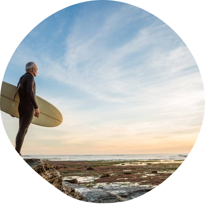 Surfer holding a longboard on a beach at sunrise, looking out over the shore and ocean