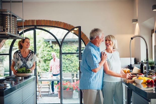 People chatting in a bright kitchen with fruit on the counter and open doors to a garden.