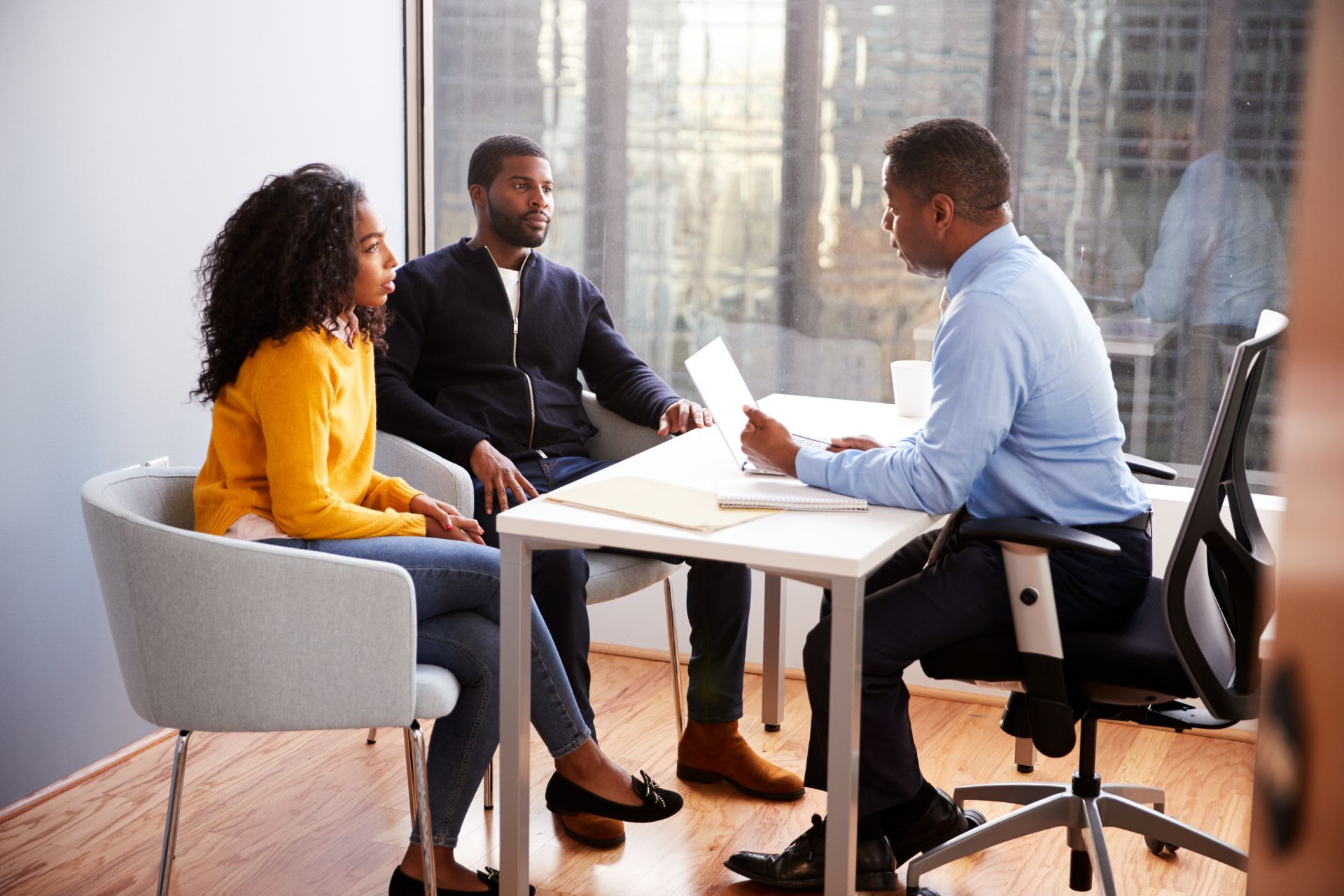 Couple and financial advisor at a desk, reviewing documents. They are sitting in a well-lit office.