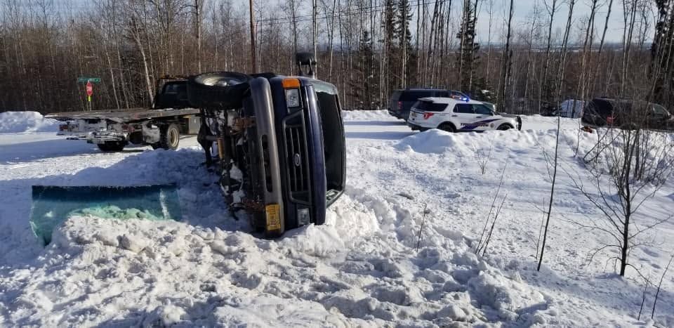 Overturned yellow vehicle in snowy ditch beside a road, with another car nearby.