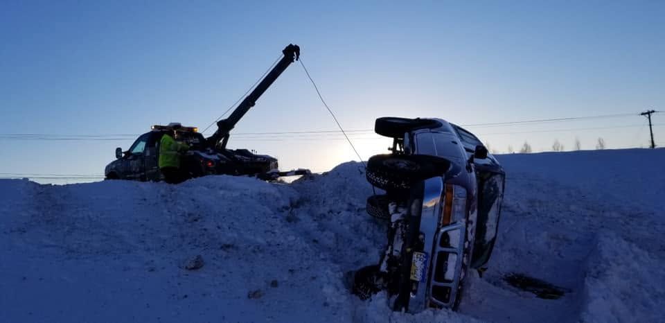 Tow truck pulling a car from a snowy ditch at dusk