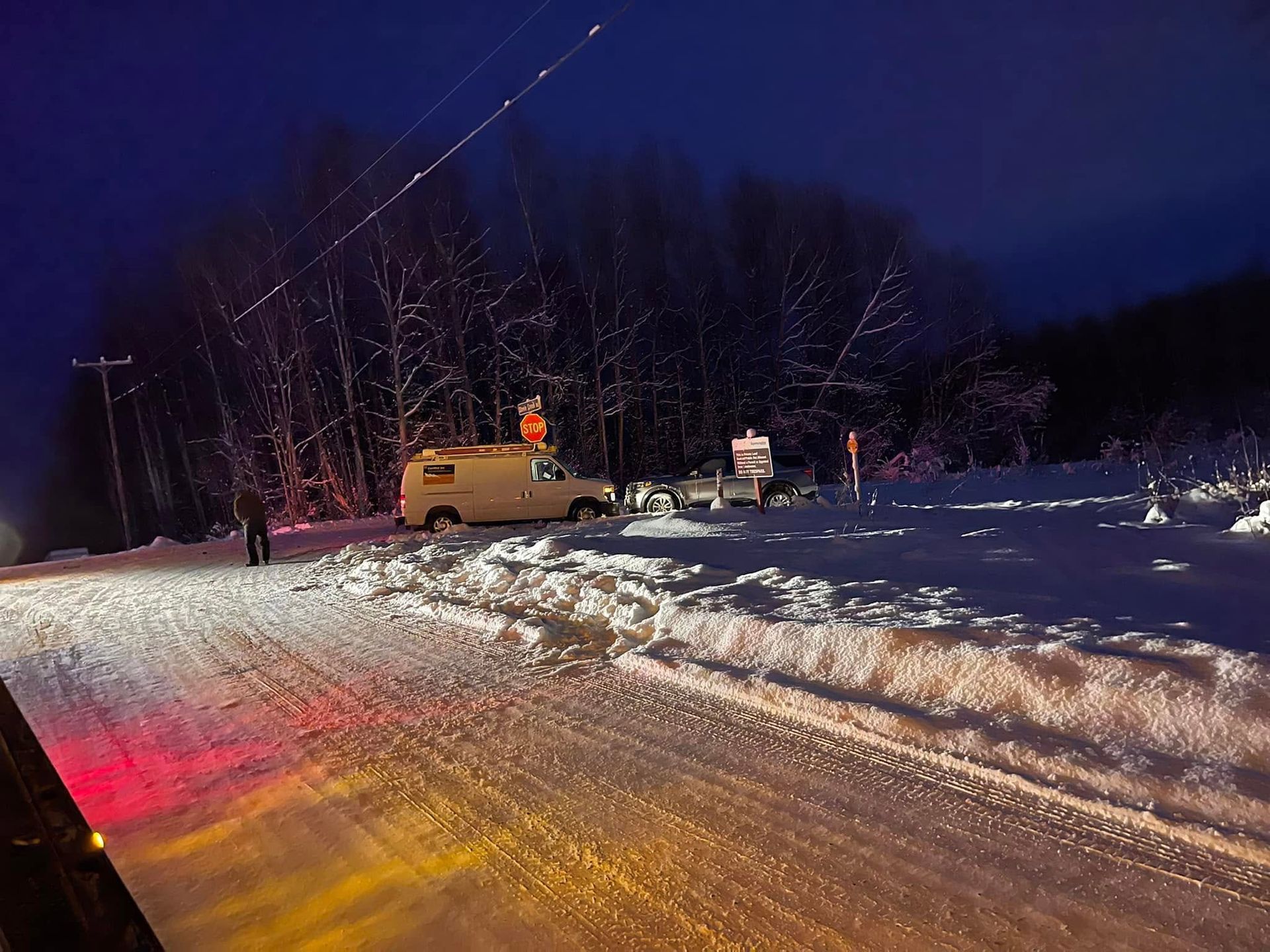 Snowy roadside at night with a pickup truck and workers near a plowed embankment