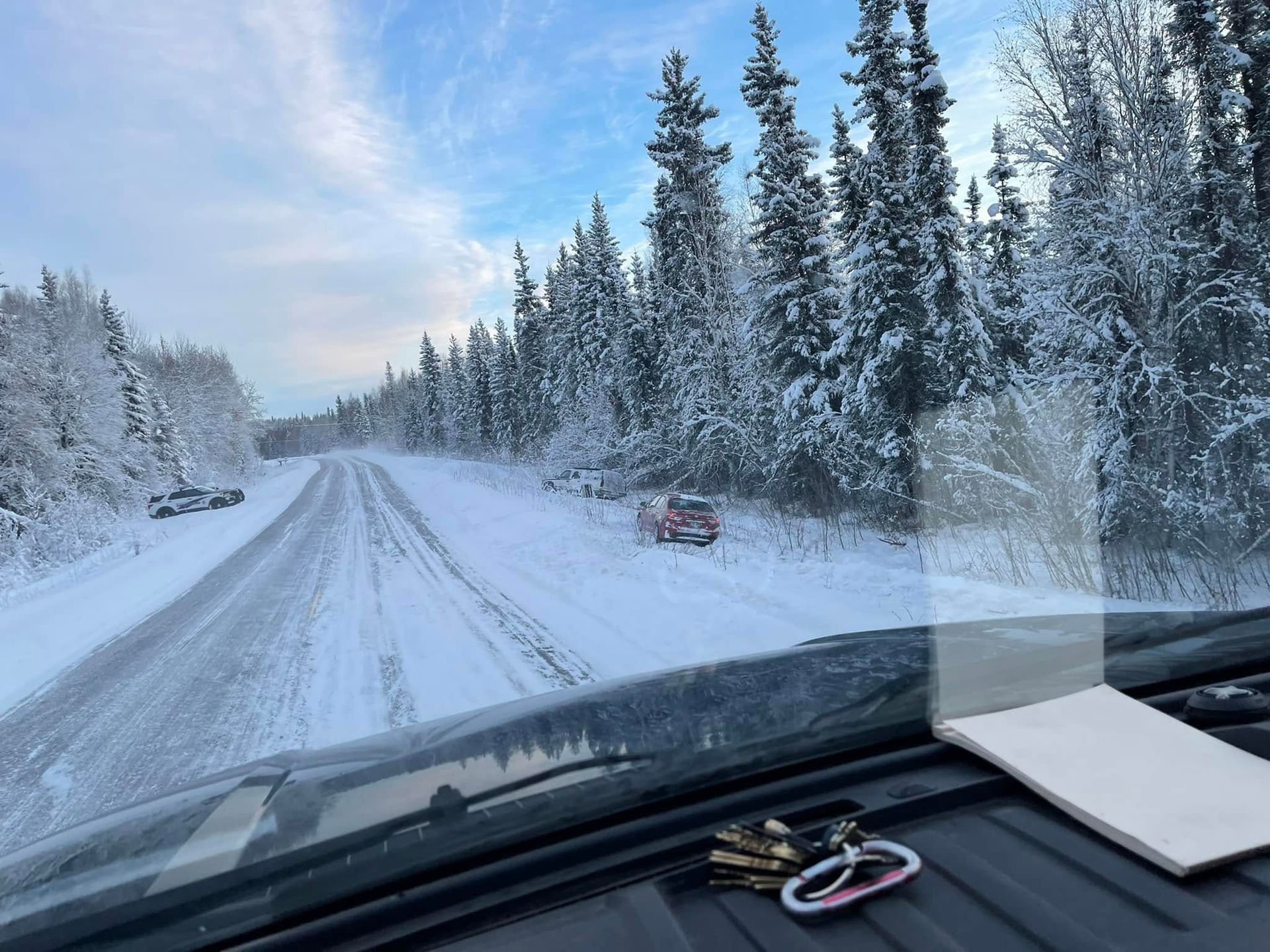 Snowy road through a winter forest, seen from inside a car with the dashboard visible.