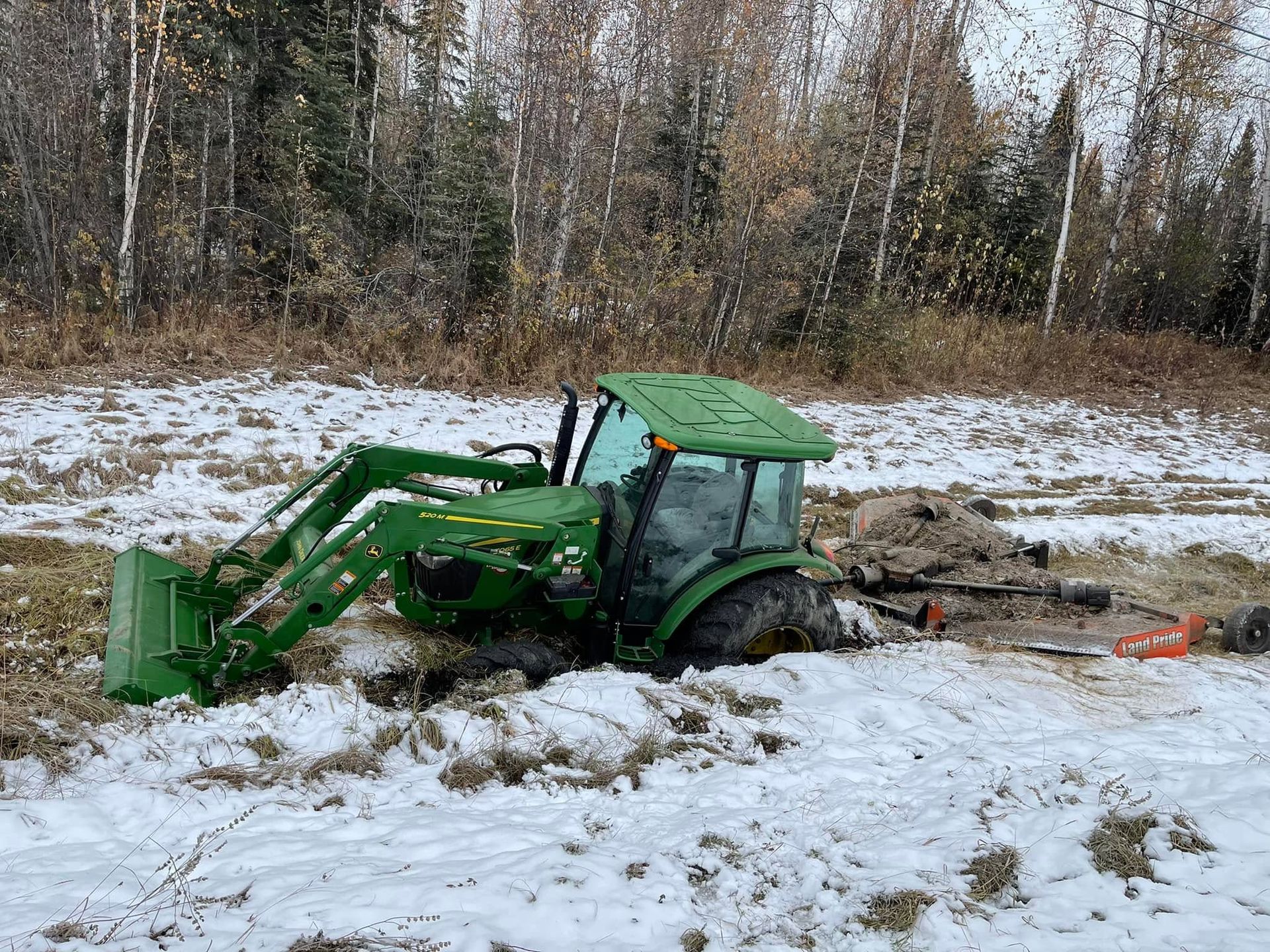 Green tractor stuck in snowy mud in a wooded field