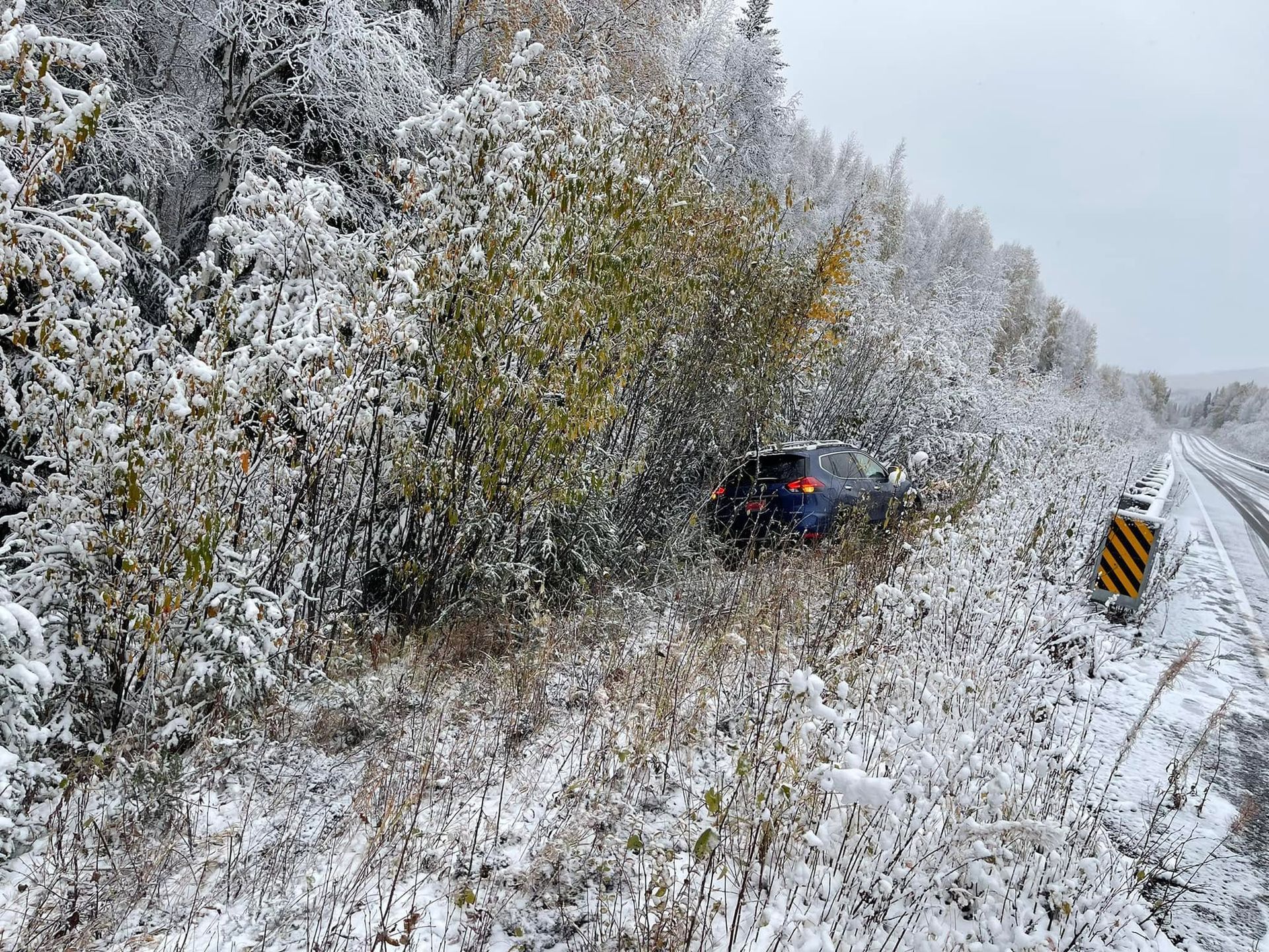Car on a snowy roadside beside trees and a black-yellow barrier marker