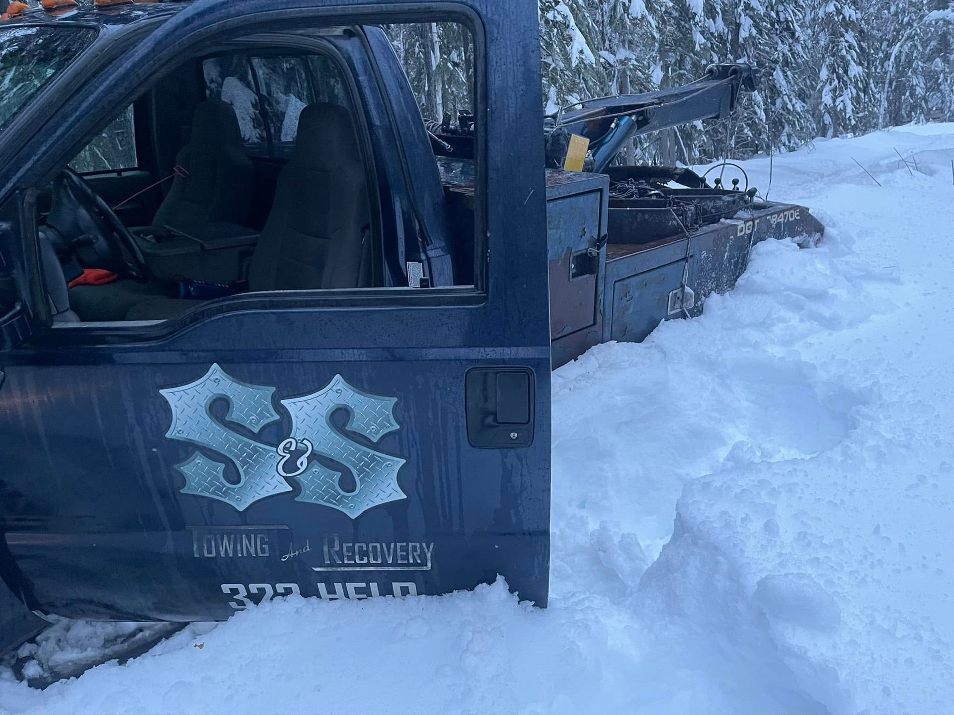 Dark blue truck stuck in deep snow beside a snowy trail in a forest