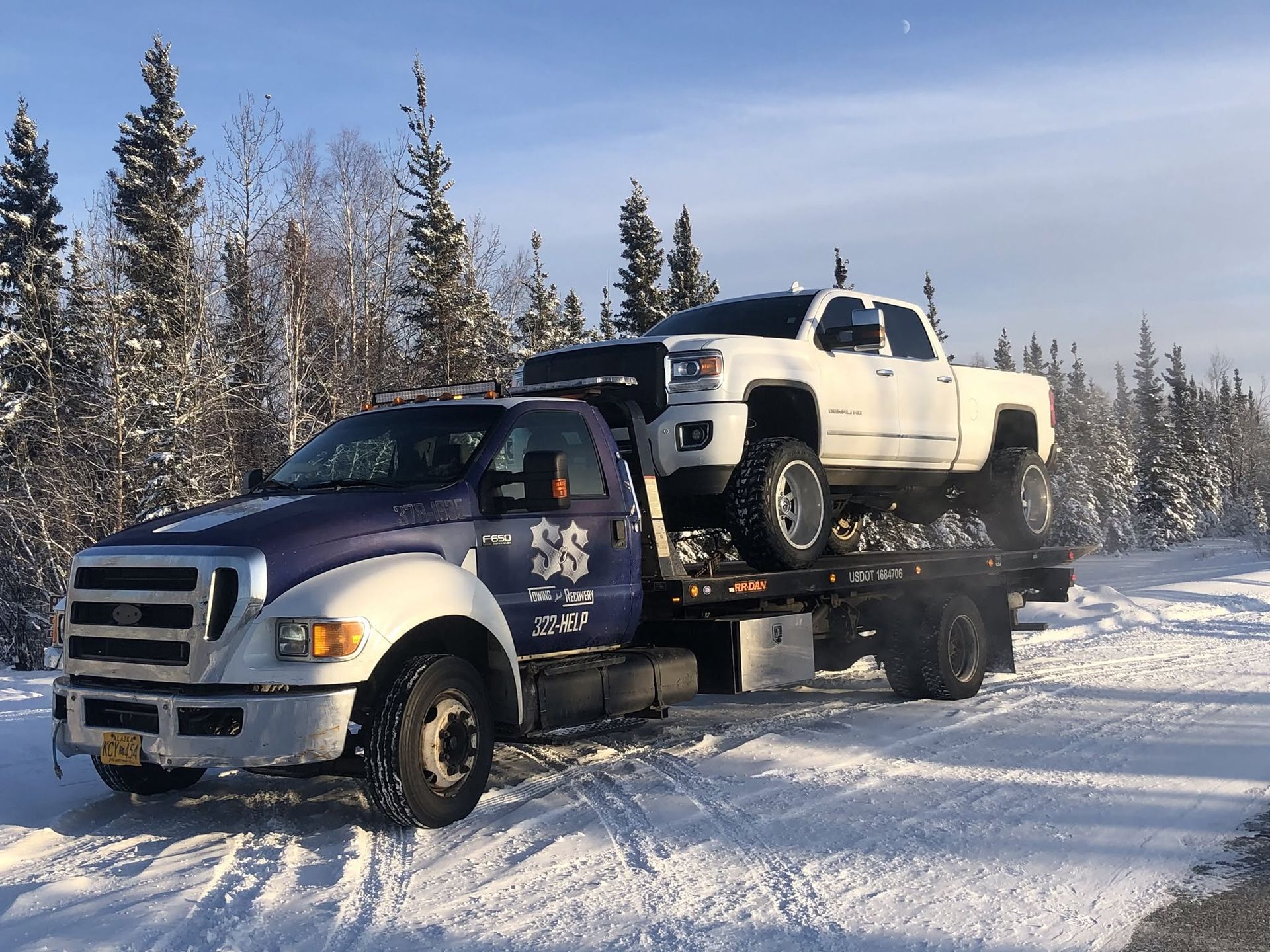 Tow truck hauling a white pickup on a snowy forest road in winter