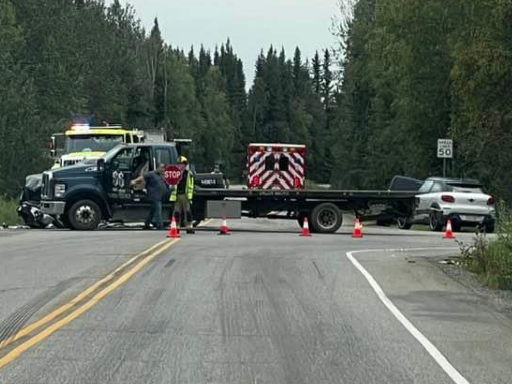 Police roadblock with tow truck, cones, and officers blocking a forest road near a stopped car.