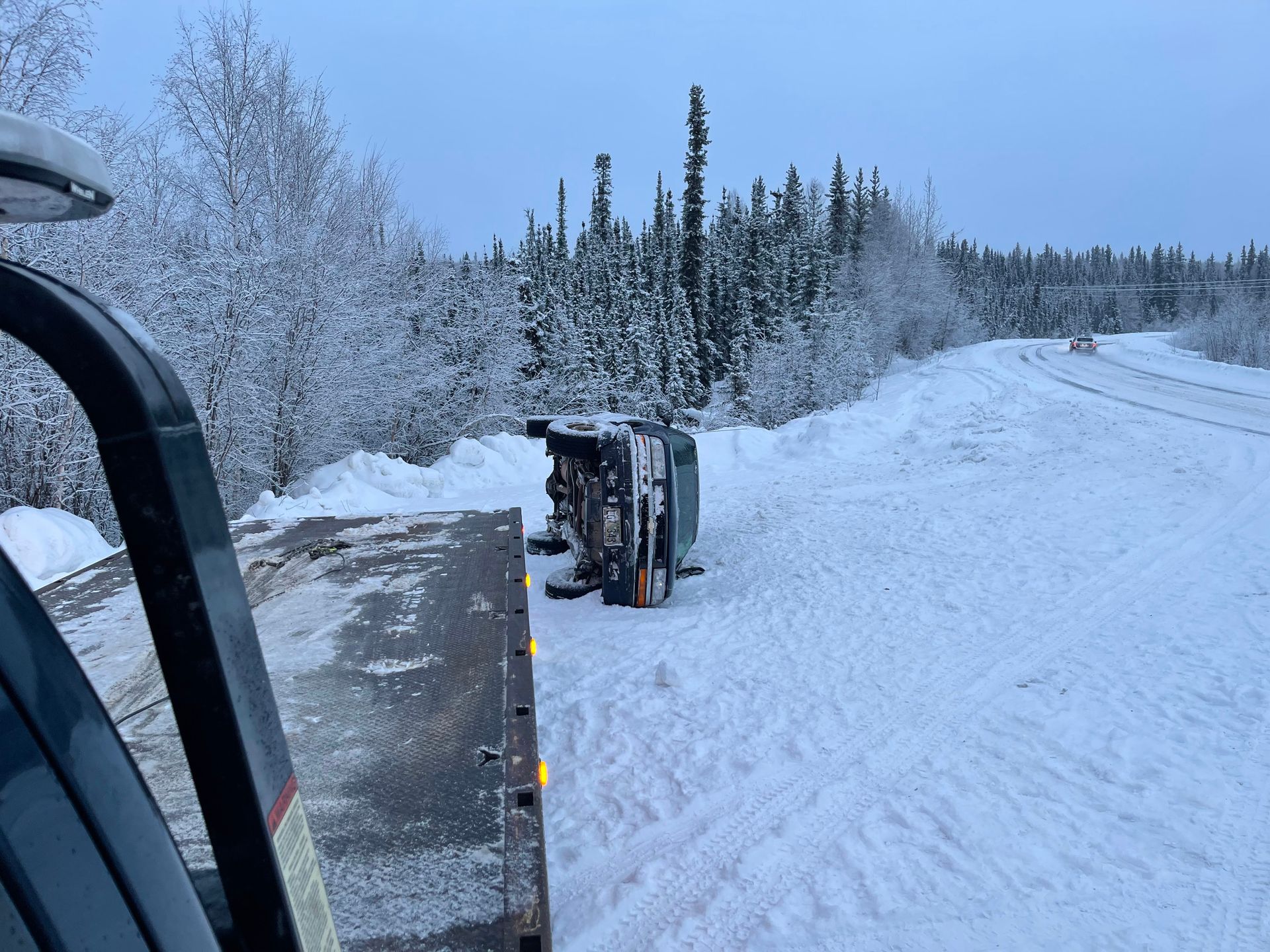 Snow-covered road beside heavy machinery in a winter forest.