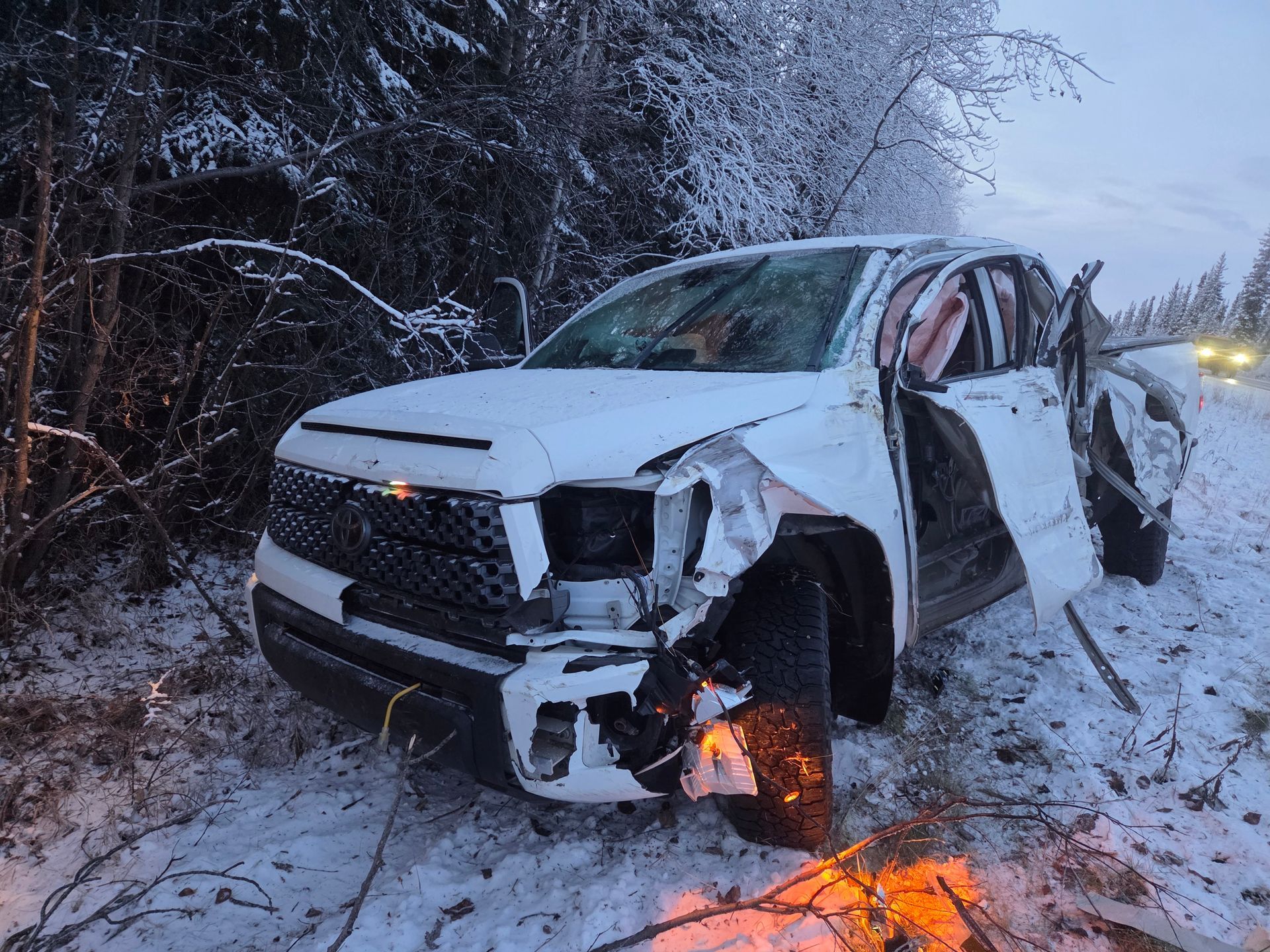 Damaged white SUV in snowy ditch with front-end fire and crumpled passenger side
