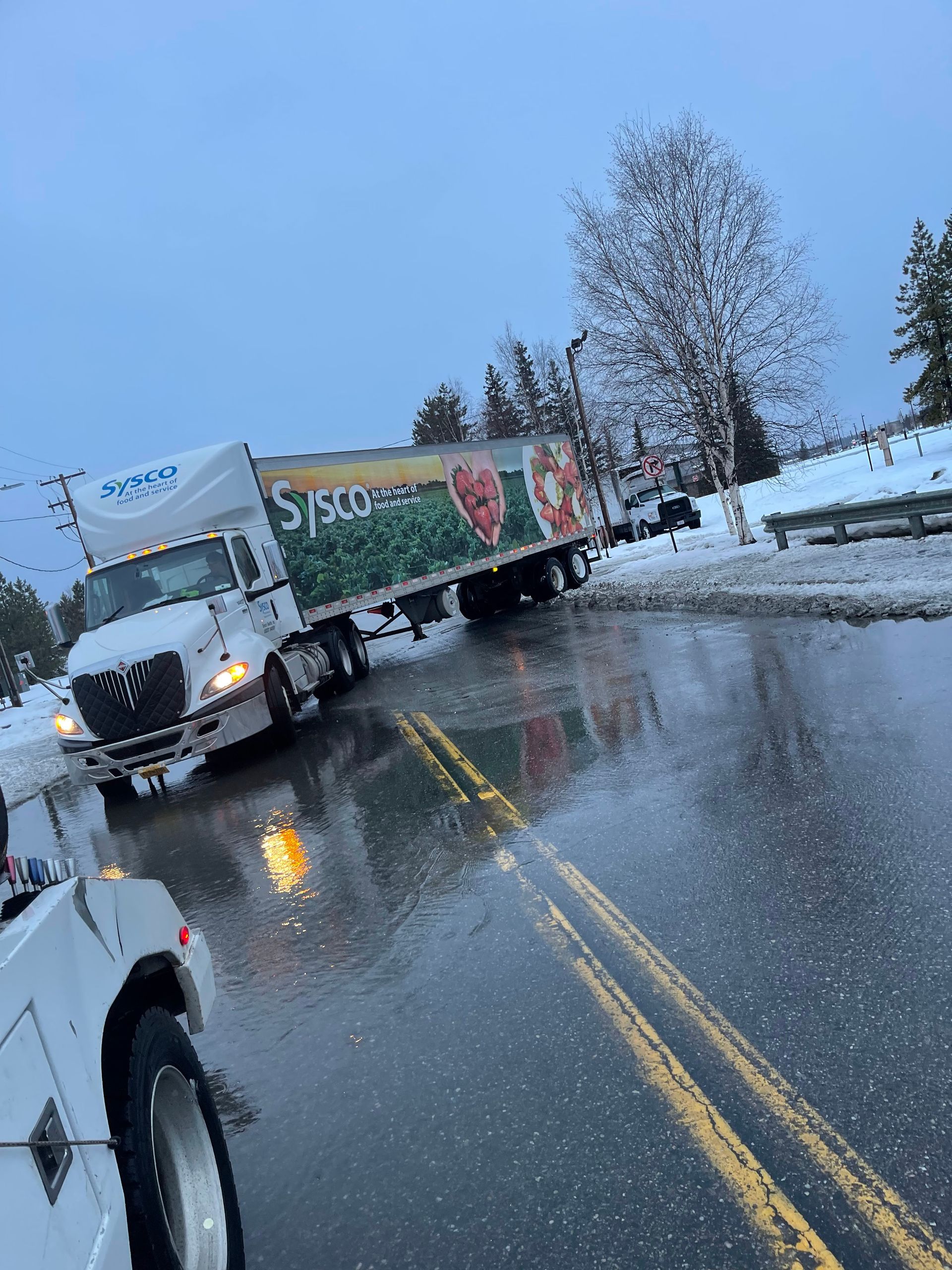 Truck jackknifed on a wet road in the snow, blocking lanes near a curb.