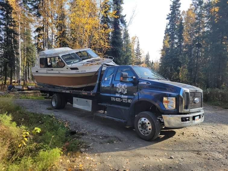 Blue pickup truck towing a small boat on a trailer along a forest dirt road
