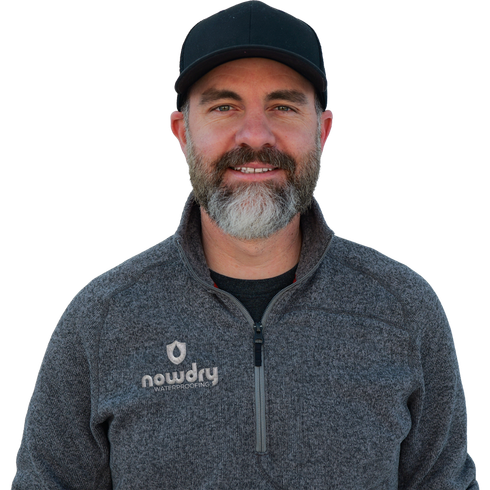 Smiling man in a black cap and gray zip-up jacket against a white background