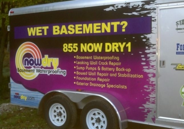 Purple trailer advertising wet basement waterproofing with “Wet Basement? 855 NOW DRY1” text